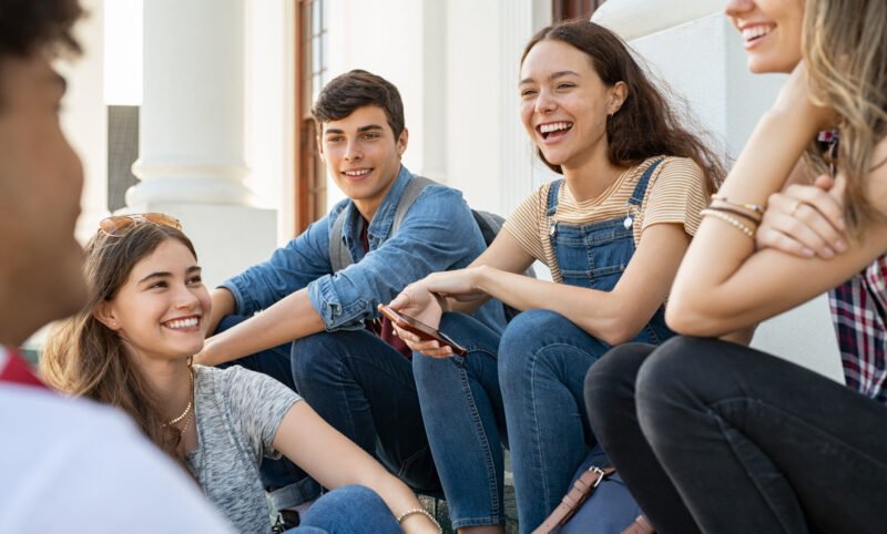 Group of happy young friends sitting in campus and talking.
